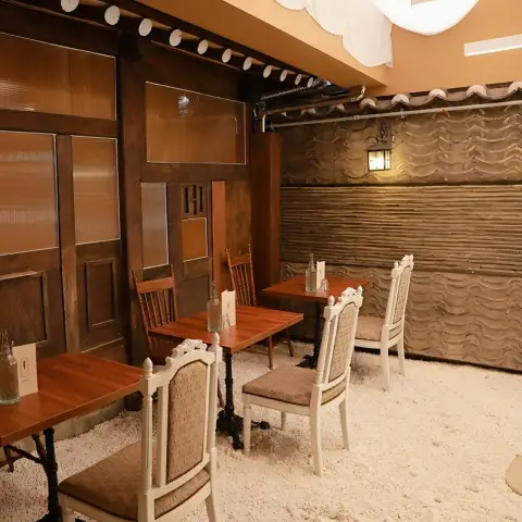 A cozy dining area with wooden tables and chairs on a white pebble floor, featuring traditional hanok walls and modern lighting.