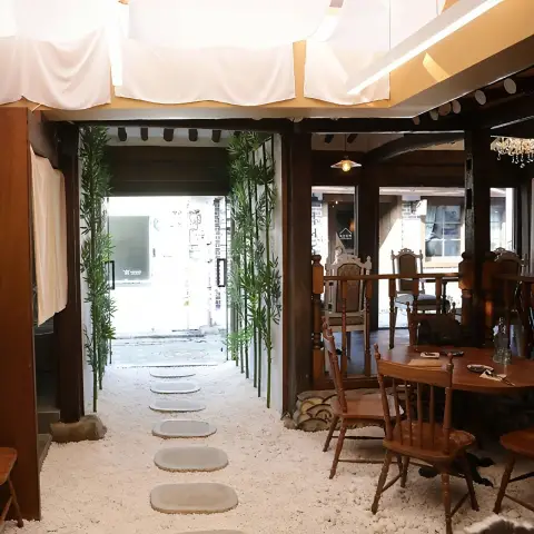The inviting entrance pathway of Ikseon-Chwihyang, featuring a white pebble ground, stepping stones, and decorative bamboo plants leading into the restaurant.