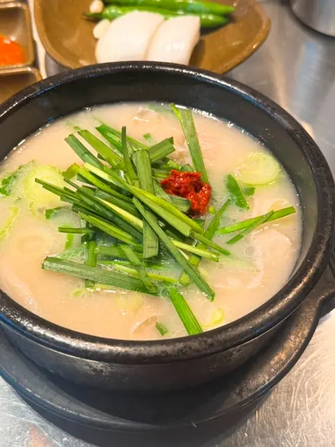 A traditional bowl of dwaeji gukbap topped with chives and red chili paste in Busan