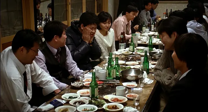 A group of people at a Korean company dinner with soju bottles on the table