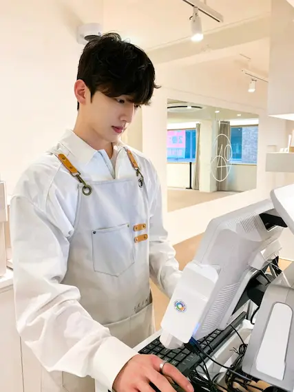Good-looking barista in a white shirt and apron using a point-of-sale system.