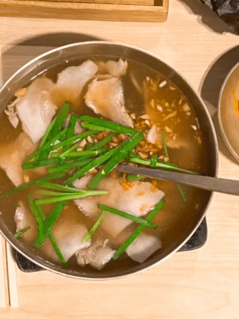 A top-down view of a bowl of Suyuk-gukbap, a Korean pork and rice soup with clear broth, garnished with chives and minced garlic.