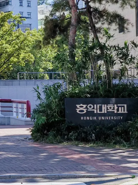 Main gate of Hongik University surrounded by trees
