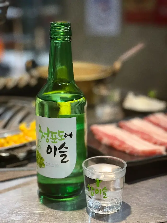 A bottle of green grape-flavored soju next to a Korean BBQ grill