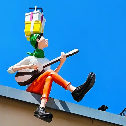 Rooftop guitarist statue balancing colorful gift boxes against a clear blue sky