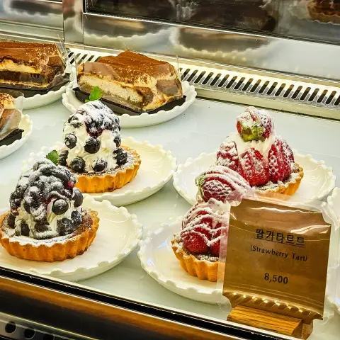 Berry tarts piled high with strawberries, blueberries, and cream in a pastry case