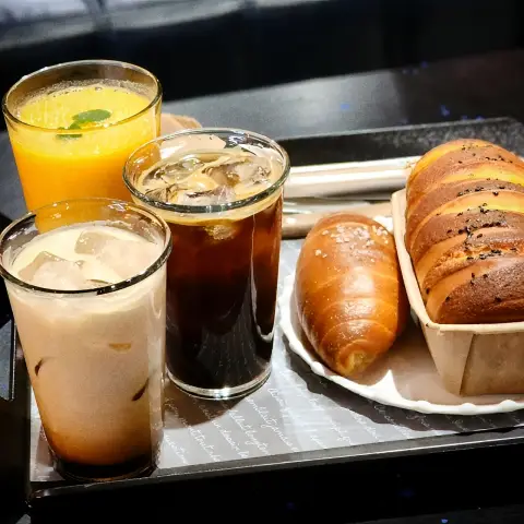 Close‑up of iced drinks with a croissant roll and pull‑apart salt bread on a tray