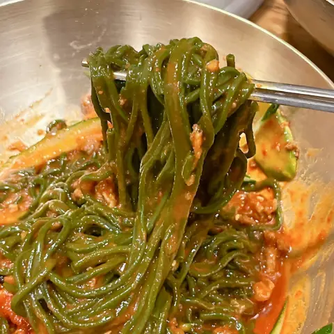 Spicy bibim guksu with green chlorella noodles lifted by chopsticks