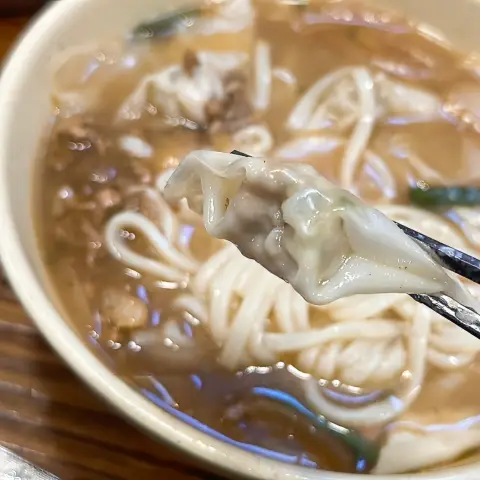 Chopsticks holding a single small dumpling over kalguksu bowl