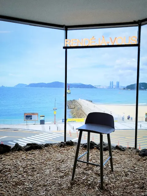 rendeja-vous-haeundae-stool-window.webp Ocean-view café interior with a stool in front of a large window at Rendeja Vous Haeundae