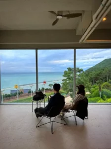 Couple seated at Cheongsapo cafe window with ocean view