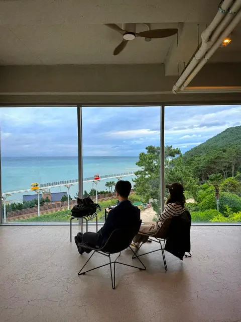 Couple seated at Cheongsapo cafe window with ocean view
