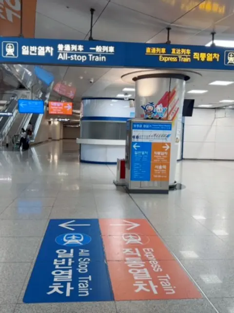 arex-station-signage-guide.webp Directional signs guiding passengers to All-Stop and Express Trains