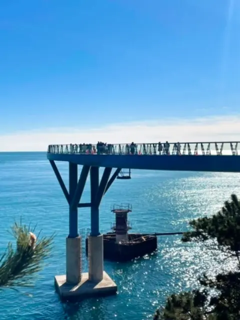 People walking on the extended glass bridge above the sea