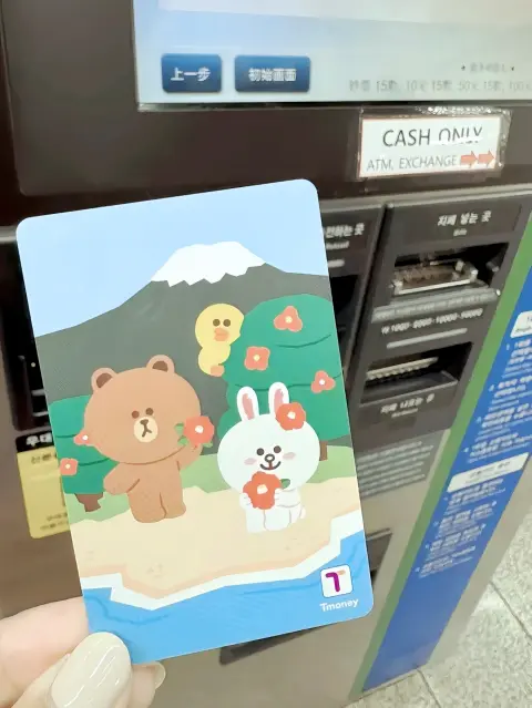 Korea T-Money card with Line Friends design held in front of a subway recharge machine
