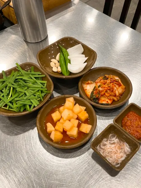 Variety of side dishes for gukbap including garlic, kimchi, chives, and dipping sauces
