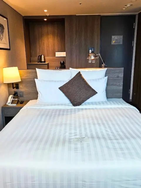 Deluxe double room bed with modern wooden interior at Kent Hotel Gwangalli by Kensington