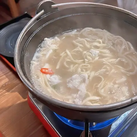 Udon cooking in hot broth with meat and chili