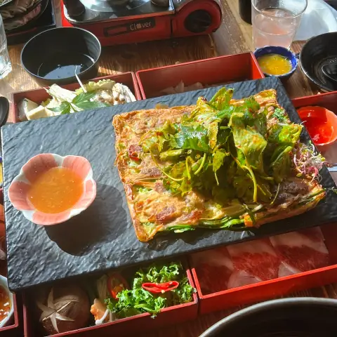 Savory Korean pancake topped with greens and dipping sauce
