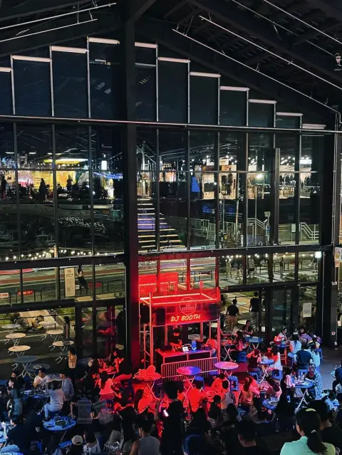 Millac The Market DJ booth at night with lively crowd and glass backdrop