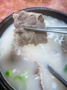 Thin beef slice lifted with chopsticks over milky broth – Imun Seollongtang