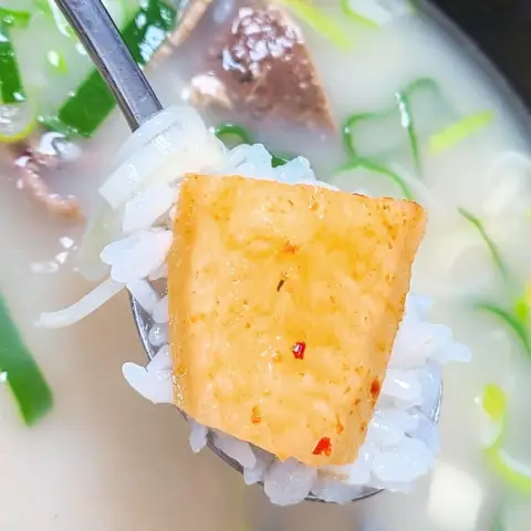 Spoonful of rice topped with kkakdugi over beef-bone soup