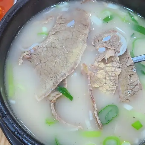 Beef slices resting in a pale broth with spring onions
