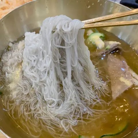 Chopsticks lifting naengmyeon noodles from the broth at Gangnam Myeonok Insadong