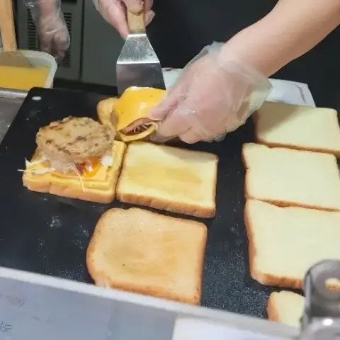 Isaac Toast Myeongdong assembly on the grill with spatula placing patty over cheese and egg
