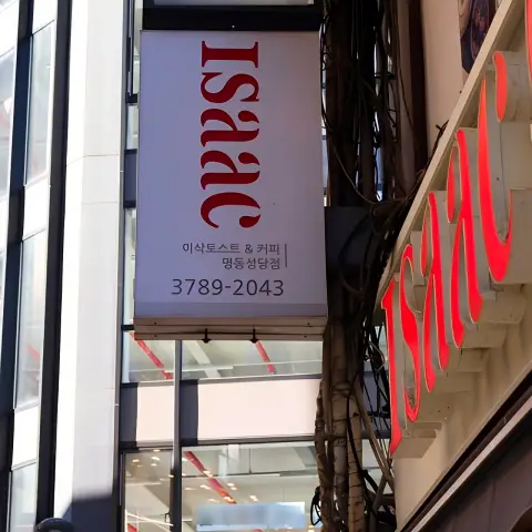 Vertical store sign with ISAAC logo and phone number along a narrow Myeongdong alley