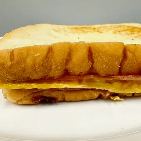Side view of a classic toast on a white plate with egg and ham