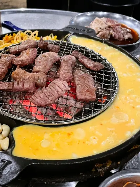 Charcoal grill filled with sizzling pork and bubbling egg