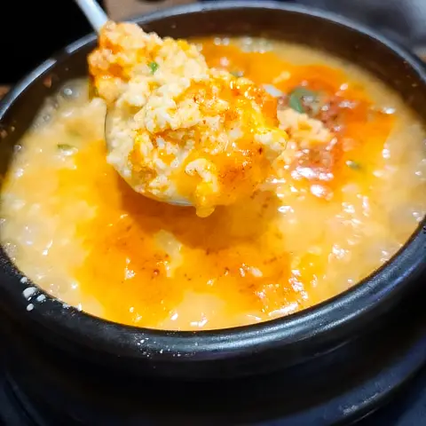 Spicy orange Sundubu-jjigae topped with a swirl of rich orange oil.